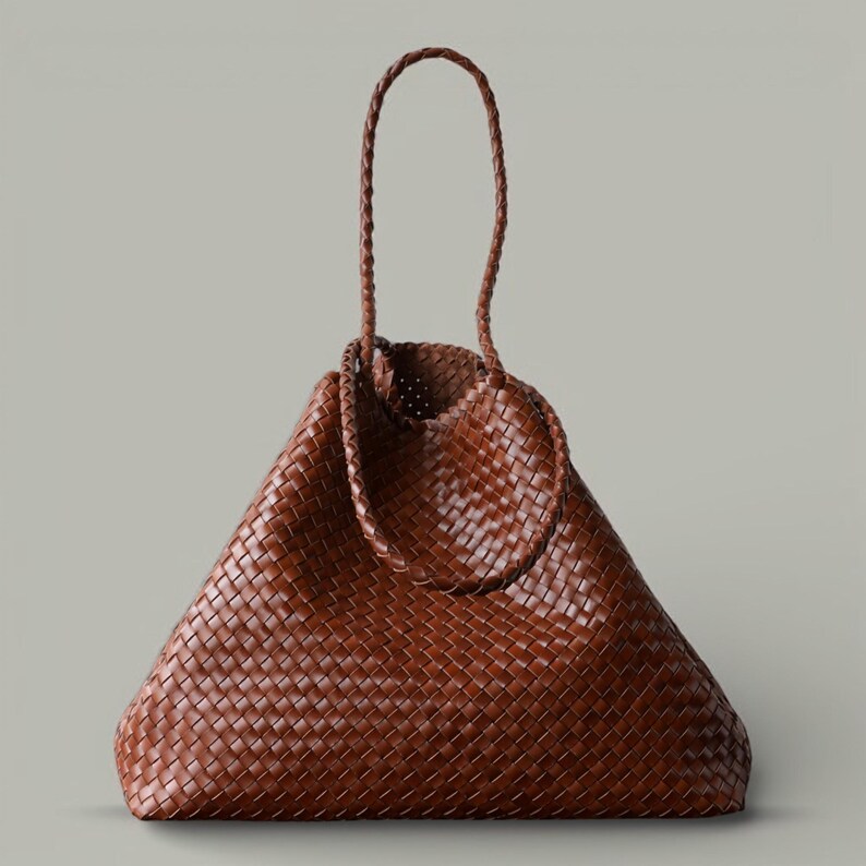 May include: A brown woven tote bag with a triangular shape. The bag features a braided handle and a woven design throughout. The bag is made of a brown material and has a spacious interior.