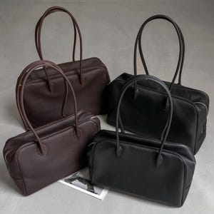 Può includere: Quattro borse tote in pelle, nei toni del marrone e del nero. Ogni borsa ha una forma rettangolare con chiusura a zip e manici lunghi e sottili. Le borse sono disposte su uno sfondo neutro, mostrando il loro design e la loro texture.