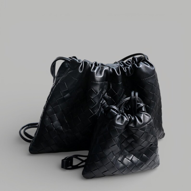 May include: Two black drawstring bags with a woven design. The larger bag has backpack straps, and the smaller bag has a single handle. Both bags are made of a soft, textured material.
