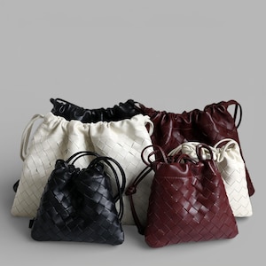 May include: A selection of woven leather drawstring bags in black, cream, and burgundy. The bags feature a basket weave design and a drawstring closure. The bags are of varying sizes. The image shows a collection of bags.