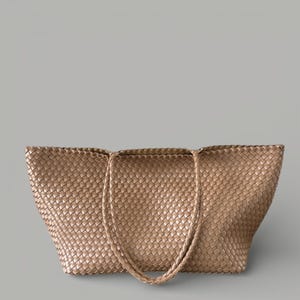 May include: A woven tote bag in a light brown color. The bag features a large, open design with two handles. The weave pattern is visible throughout the bag's exterior.