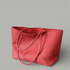 May include: A red woven tote bag with braided handles. The bag has a rectangular shape and a textured surface. The handles are long enough to be worn over the shoulder. The bag is made of a durable material.