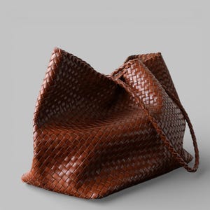 May include: A large, brown woven leather tote bag. The bag features a braided shoulder strap and a spacious interior. The leather has a rich, warm tone, and the weave pattern is tightly constructed.