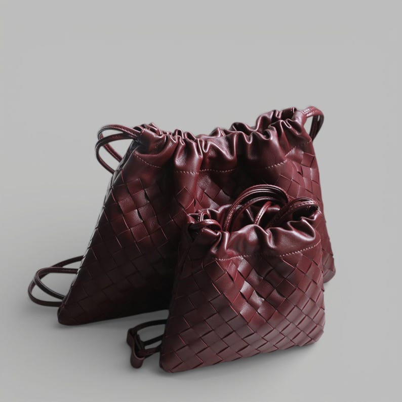 May include: Three burgundy drawstring bags of different sizes. The bags have a woven texture and a gathered top with a handle. The bags are made of a smooth, leather-like material.