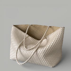 May include: Off-white woven tote bag with braided handles. The bag features a spacious interior and a textured, basket-weave design. The neutral color and simple design make it a versatile accessory for everyday use.