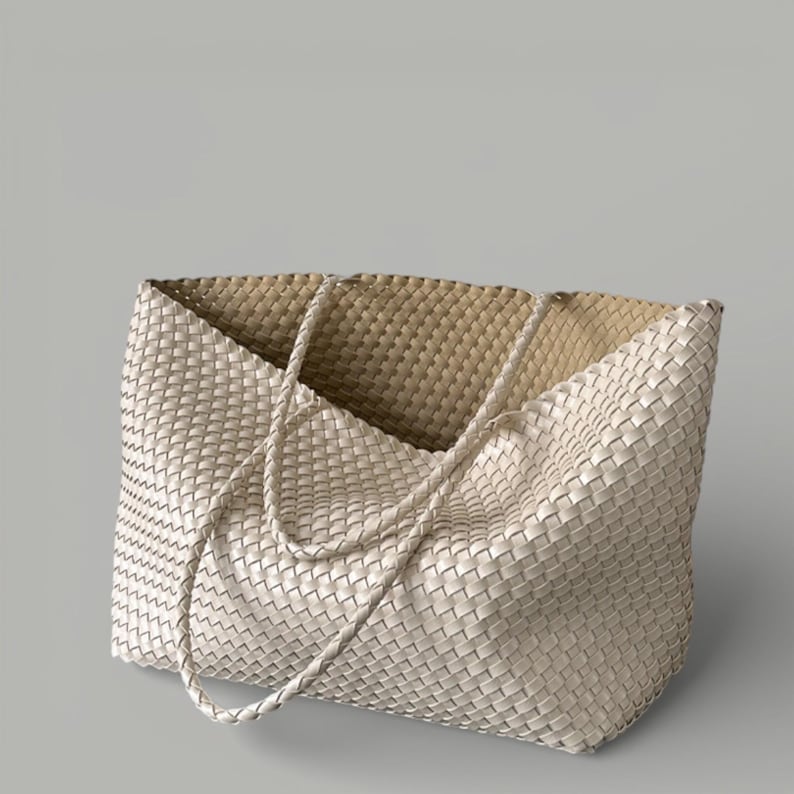 May include: Off-white woven tote bag with braided handles. The bag features a spacious interior and a textured, basket-weave design. The neutral color and simple design make it a versatile accessory for everyday use.