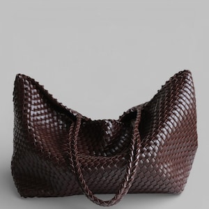 May include: A large, dark brown woven leather tote bag. The bag features a braided handle and a spacious interior. The woven pattern is consistent throughout the bag, creating a textured appearance. The bag is designed for carrying items.