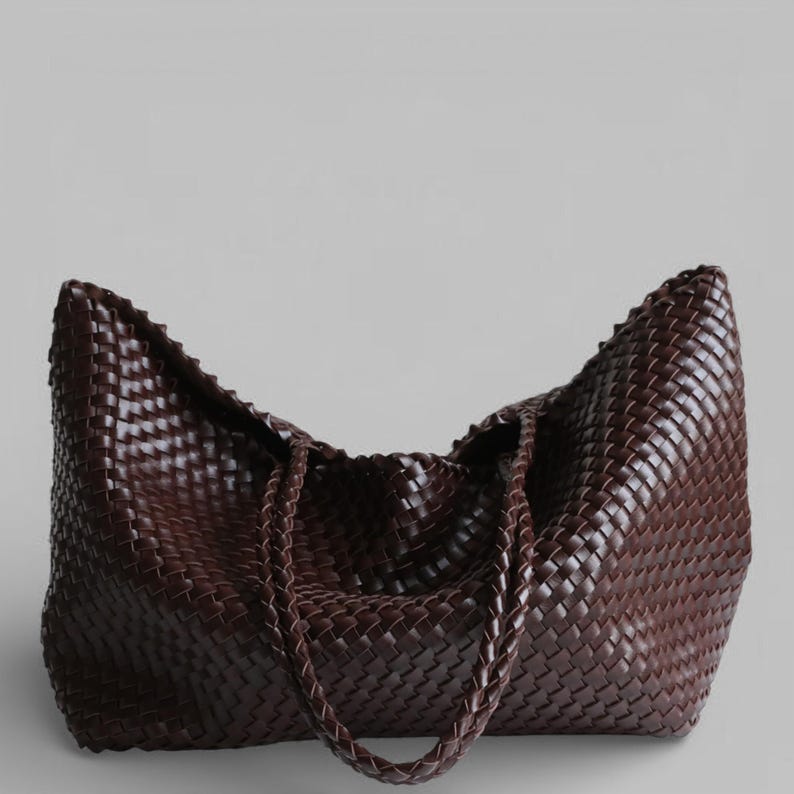 May include: A large, dark brown woven leather tote bag. The bag features a braided handle and a spacious interior. The woven pattern is consistent throughout the bag, creating a textured appearance. The bag is designed for carrying items.