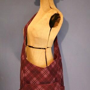 May include: A purple and gray plaid shoulder bag with a large pocket on the front. The bag is being modeled on a wooden mannequin.