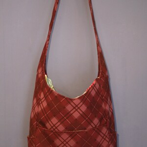 May include: A red and brown plaid shoulder bag with a single strap and a front pocket.