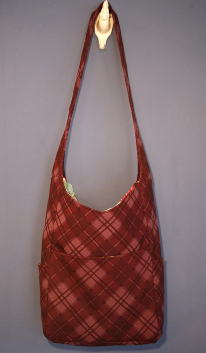 May include: A red and brown plaid shoulder bag with a single strap and a front pocket.