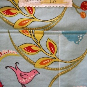 May include: A close-up of a blue and white fabric with a floral pattern. The fabric has a yellow, orange, and red floral design. The fabric has a white label with the text "SobeSata Co. Handmade purses, bags, totes, and more."
