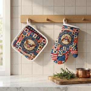 Könnte beinhalten: Ein patriotisches Küchenset mit einem Topflappen und einem Ofenhandschuh. Beide Artikel zeigen ein Patchwork-Design mit Sternen, Streifen und dem Text "Land of the Free" und "1776-2026". Das Set ist weiß eingefasst und hängt an einer Holzleiste.