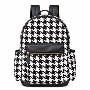 May include: A backpack featuring a black and white houndstooth pattern. The bag includes a front zipped pocket with a black leather-like trim, two side pockets, a top handle, and adjustable black shoulder straps with gold-toned metal hardware.