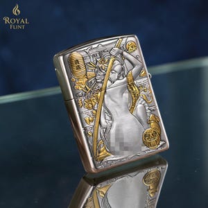 May include: Silver and gold-toned metal lighter with an engraved design. The design features a woman with a sword, floral elements, and a lantern. The lighter has the words "ROYAL FLINT" and a flame logo.