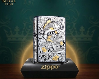 May include: A silver-toned Zippo lighter featuring an intricate black and gold engraved design of a koi fish swimming amidst stylized waves and traditional architectural structures, with gold floral accents and a hinged metal lid construction.