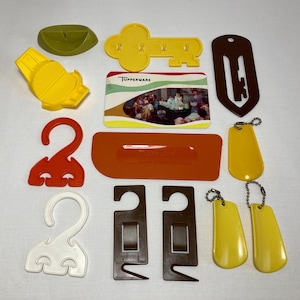 May include: A collection of various Tupperware kitchen accessories in shades of yellow, brown, orange, and white. Includes a key-shaped item, a card with a group photo, and several hooks and tags.