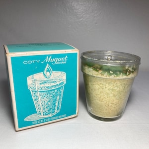 May include: A vintage Coty Muguet fragrance wax chips set. The box is teal with a white and blue illustration of a candle in a pot. The clear plastic container holds yellow wax chips. The total net weight is 5.5 oz.
