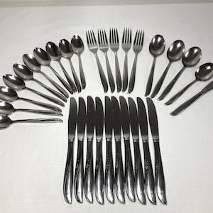 May include: A stainless steel flatware set consisting of nine spoons, five forks, eight knives, and one additional knife, all featuring a polished metallic finish and a curved handle design with a small etched floral detail at the base of each handle.