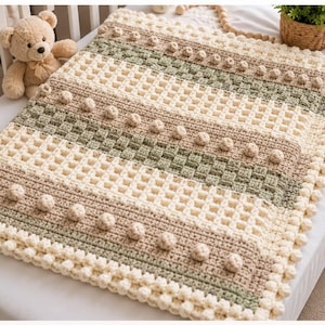 May include: A rectangular crochet blanket featuring horizontal stripes in cream, beige, and sage green. The design incorporates a waffle stitch texture and rows of raised bobble stitches. The edges are finished with a border of small bobbles.