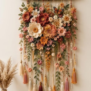 May include: A wall hanging featuring a collection of crocheted flowers in shades of rust, cream, pink, and orange, attached to a horizontal wooden branch. The arrangement includes green crocheted leaves, a butterfly, and hanging yarn tassels.