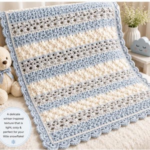 May include: A rectangular crochet blanket featuring alternating horizontal stripes of light blue and cream yarn. The design incorporates intricate openwork floral patterns and a scalloped border. A circular text overlay reads: A delicate winter-inspired texture that is light, cozy & perfect for your little snowflake!