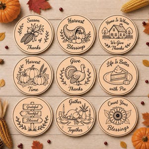 May include: A set of nine round wooden coasters featuring black line art illustrations and text related to autumn and Thanksgiving. Designs include a cornucopia, a turkey, a house, pumpkins, a slice of pie, a sunflower, and signs with grateful phrases.