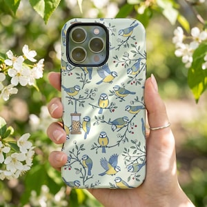 Puede incluir: Una funda de smartphone de color verde claro con un patrón repetitivo de pájaros azules y amarillos posados en ramas finas con pequeñas bayas rojas y flores blancas, incluyendo un pájaro en un comedero rectangular.