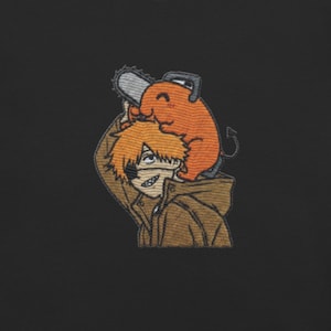 Puede incluir: Parche bordado con un personaje de estilo anime con cabello naranja y una chaqueta marrón, con una motosierra en la cabeza y una pequeña criatura naranja. El parche tiene un fondo negro.