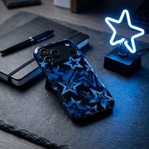 Puede incluir: Una funda para smartphone con un patrón de estrellas en azul oscuro y negro. La funda tiene un acabado brillante y cubre la parte posterior de un teléfono con un recorte para una cámara de tres lentes. El diseño consta de estrellas superpuestas.
