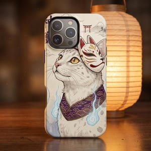 Pode incluir: Uma capa de telemóvel com um gato branco que usa uma máscara de raposa vermelha e branca na cabeça. O gato usa uma coleira roxa com padrões e detalhes de chamas azuis. O fundo creme mostra uma montanha, um torii e nuvens.