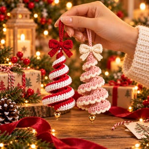 Hand holding a red and white candy cane crochet spiral tree with a red bow and a blush pink scalloped spiral tree with a cream bow