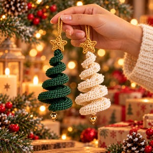 Hand holding a dark green crochet spiral tree and an ivory spiral tree with pearl beads, both with gold star toppers and gold bells