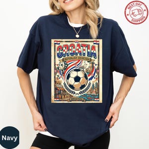 A woman wearing a navy blue t-shirt with a graphic design featuring a soccer ball, a flag, and text related to Croatia.