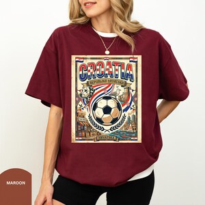 A woman wearing a burgundy t-shirt with a graphic design featuring a soccer ball, a flag, and various elements associated with Croatia.