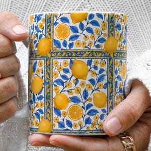 A person's hands holding a colorful mug with a pattern of lemons and flowers.