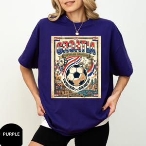 A woman wearing a purple t-shirt with a graphic design featuring a soccer ball, a flag, and various text elements related to Croatia.