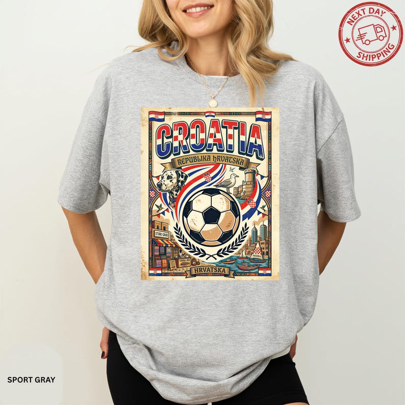 A woman wearing a gray t-shirt with a graphic design featuring a soccer ball, a flag, and various elements related to the country of Croatia.