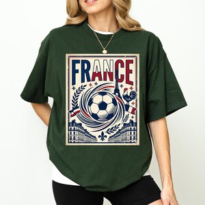 A woman wearing a green t-shirt with a graphic design featuring a soccer ball, a rooster, and various French-themed elements.