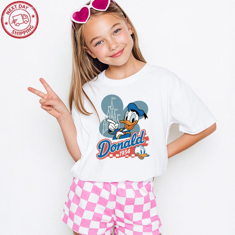 A young girl wearing a white t-shirt with a Disney character and a peace sign, smiling and posing for the camera.
