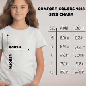 Puede incluir: Una camiseta blanca con una tabla de tallas para Comfort Colors 9018. La tabla muestra las tallas XS a XL, con medidas de ancho y largo en pulgadas. La camiseta la lleva una persona.