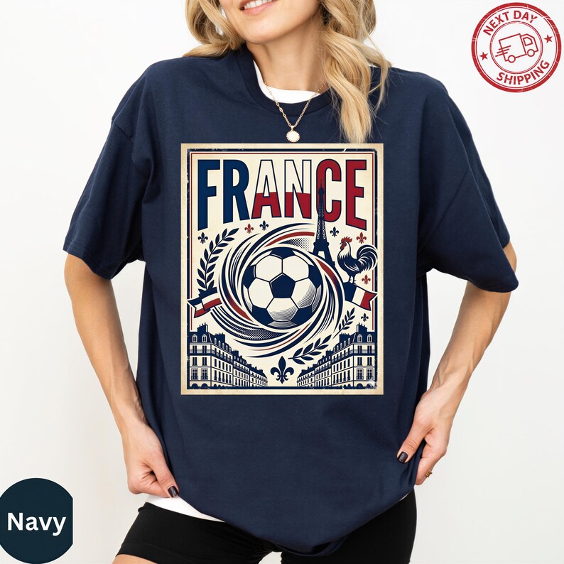 A navy blue t-shirt with a graphic design featuring a soccer ball, a rooster, and various architectural elements, along with the word "FRANCE" prominently displayed.