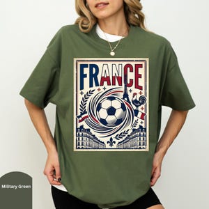 A woman wearing a green t-shirt with a graphic design of a soccer ball and various landmarks, including the Eiffel Tower, surrounded by the word "FRANCE".