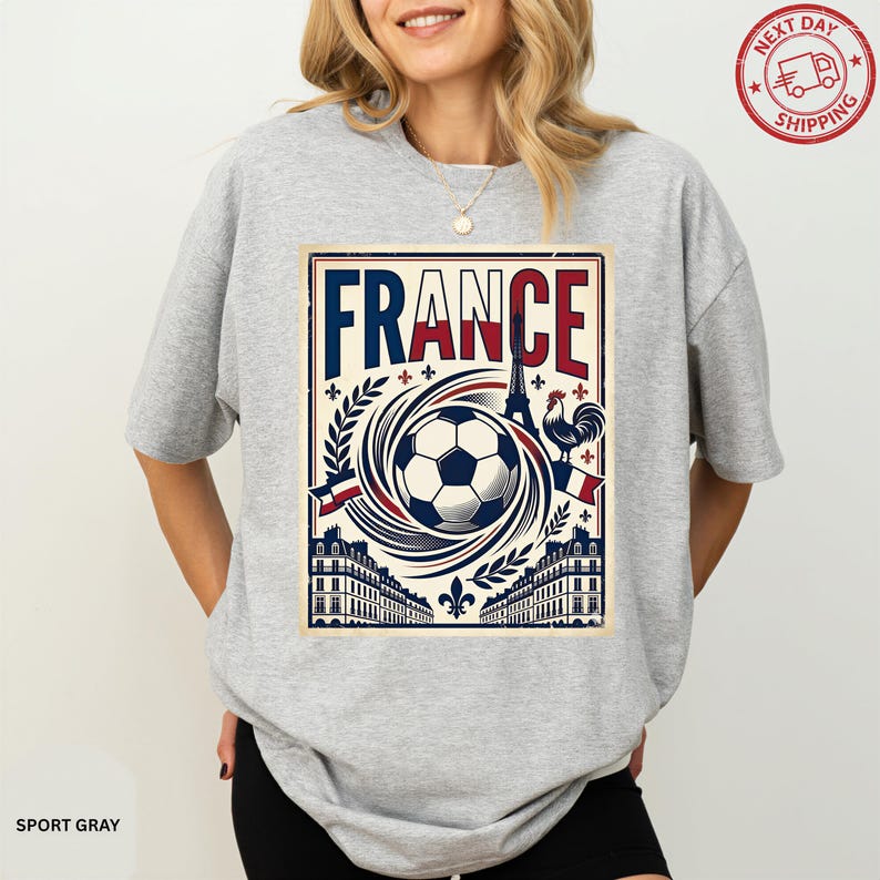 A woman wearing a grey t-shirt with a graphic design featuring the word "FRANCE" and various soccer-related elements.