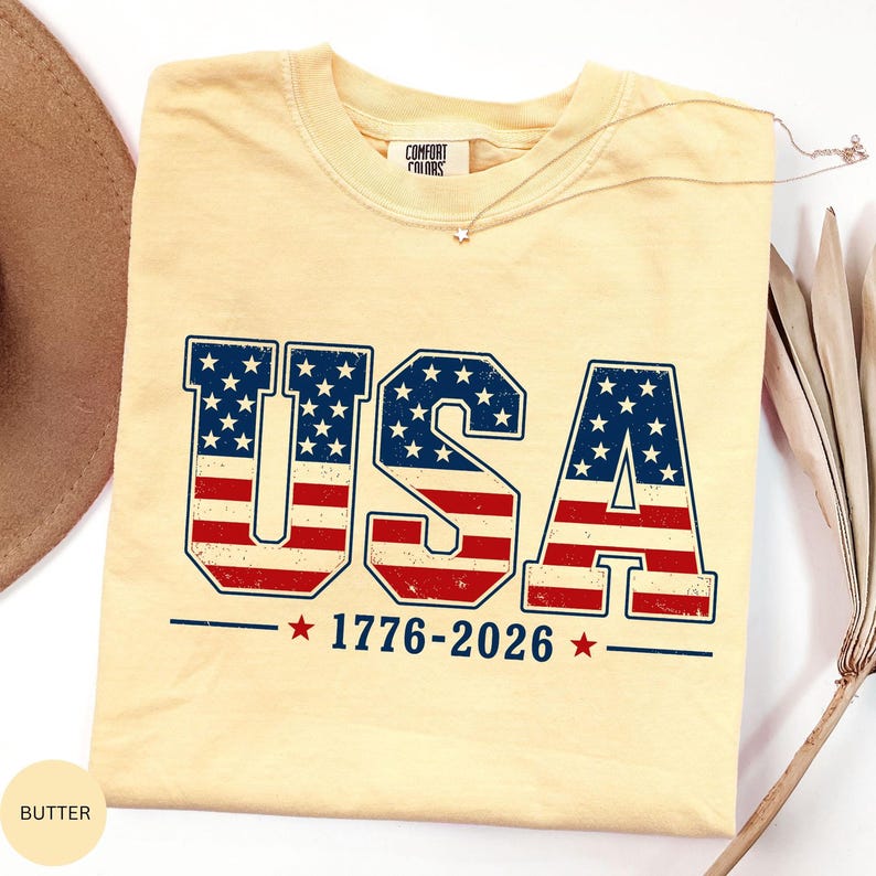 A yellow t-shirt with the text "USA" and "1776-2026" printed on it, along with an American flag design.