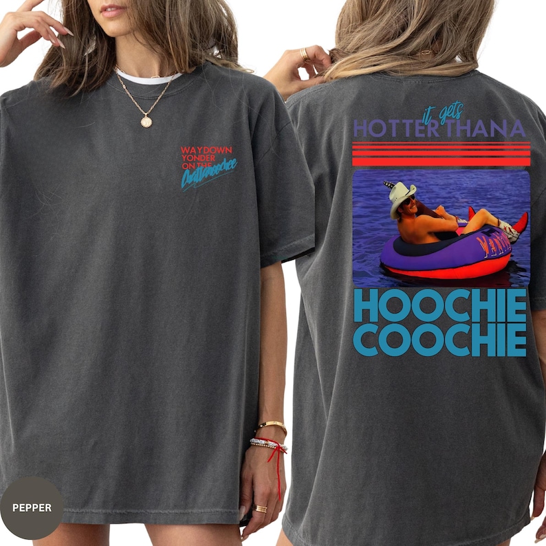 Puede incluir: Camiseta gris oscuro con el texto "WAYDOWN YONDER on the Chattahoochee" en rojo y azul en la parte delantera. La parte trasera muestra un gr&aacute;fico de una persona en un flotador con el texto "It gets HOTTER than a HOOCHIE COOCHIE".