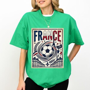 A woman wearing a green t-shirt with a graphic design featuring a soccer ball, buildings, and a rooster, along with the word "FRANCE" prominently displayed.