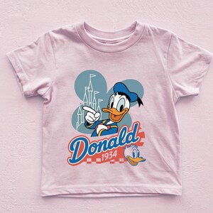 A pink t-shirt with a cartoon image of Donald Duck and the text "Donald 1934" printed on it.