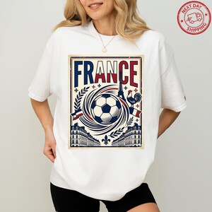 A woman wearing a white t-shirt with a graphic design featuring the word "FRANCE" and various elements associated with the country, such as a soccer ball, buildings, and a rooster.