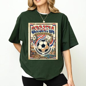 A woman wearing a green t-shirt with a graphic design featuring a soccer ball, a flag, and various landmarks, along with the text "Cratia Republika Republika" and "HRVSA".